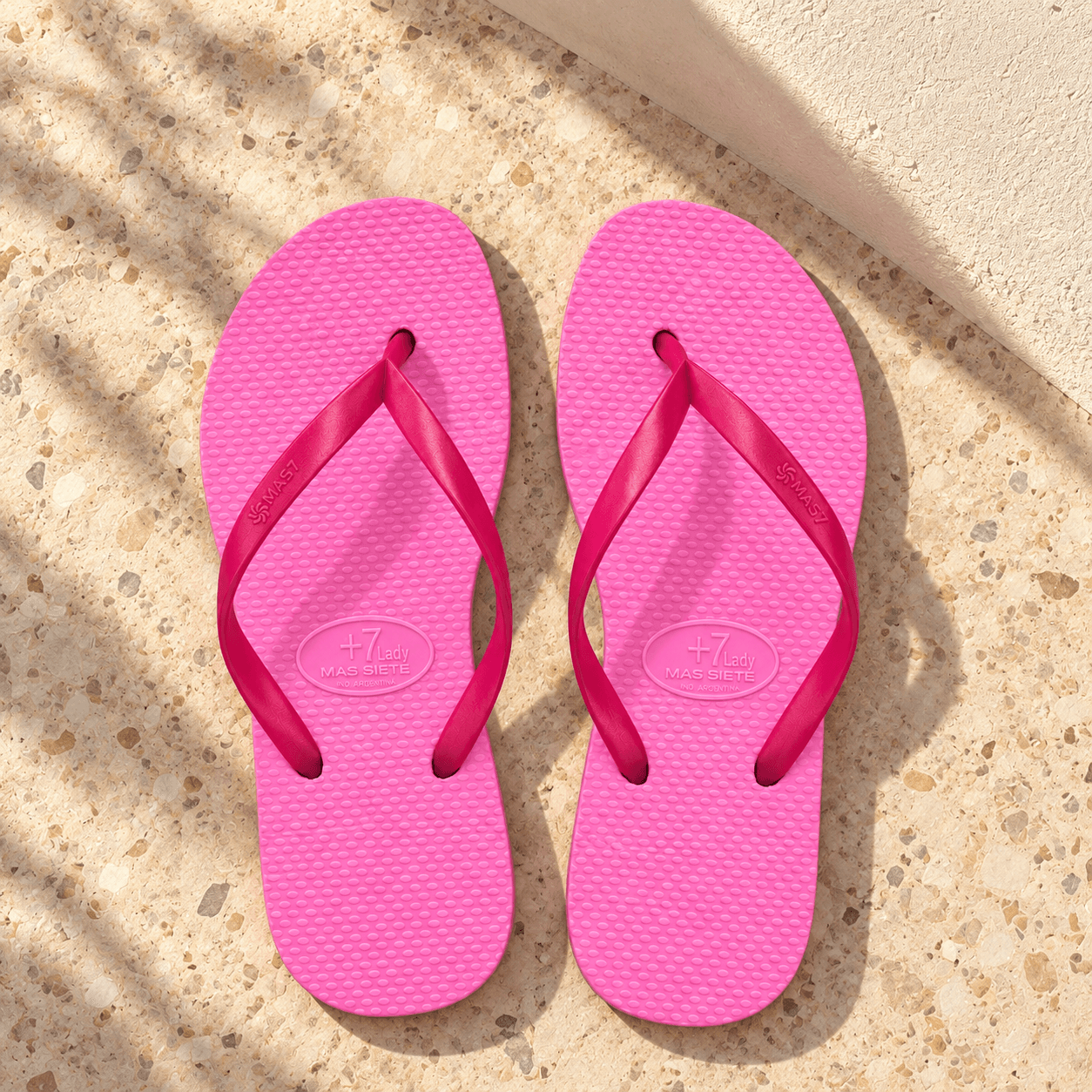 Un par de ojotas Fucsia en una terraza luminosa de verano, sin personas ni accesorios.