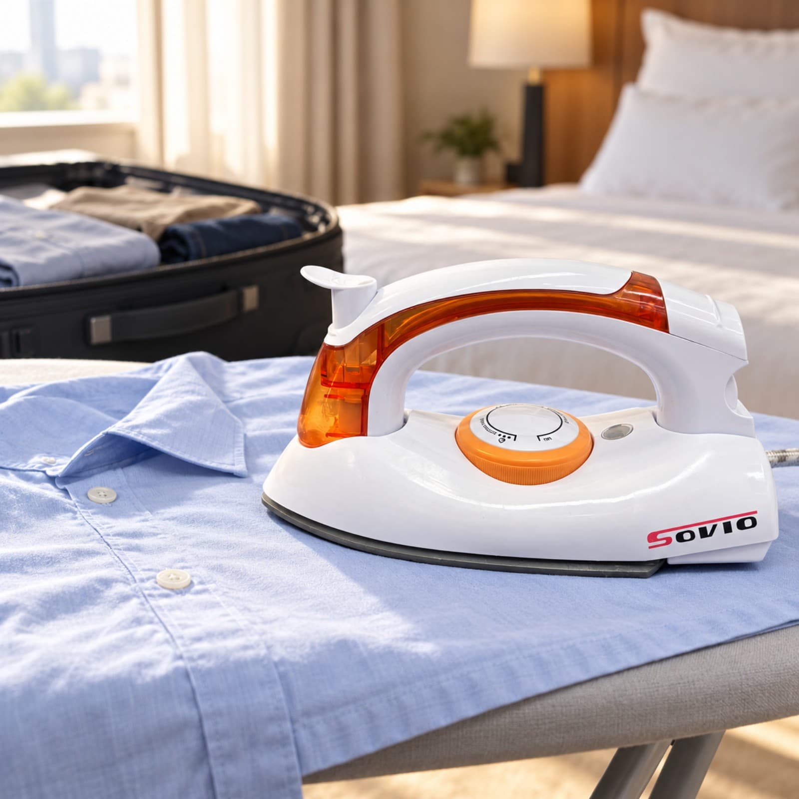 Plancha de viaje Sovio S-258B naranja apoyada sobre una camisa en una tabla de planchar, en una habitación de hotel con una valija abierta (imagen ilustrativa) — miniatura 5